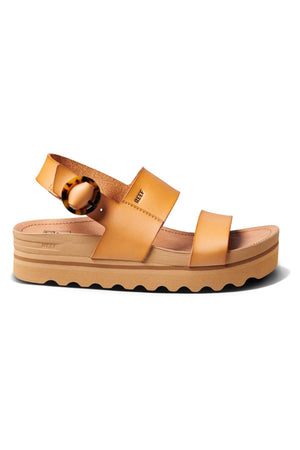 The REEF Vista Hi Buckle sandals boast a tan platform with two wide straps of vegan leather upper across the toe and midfoot, an adjustable ankle strap adorned with a tortoiseshell buckle, and a grooved beige sole. The thick, contoured footbed is designed to provide excellent arch support for enhanced comfort.