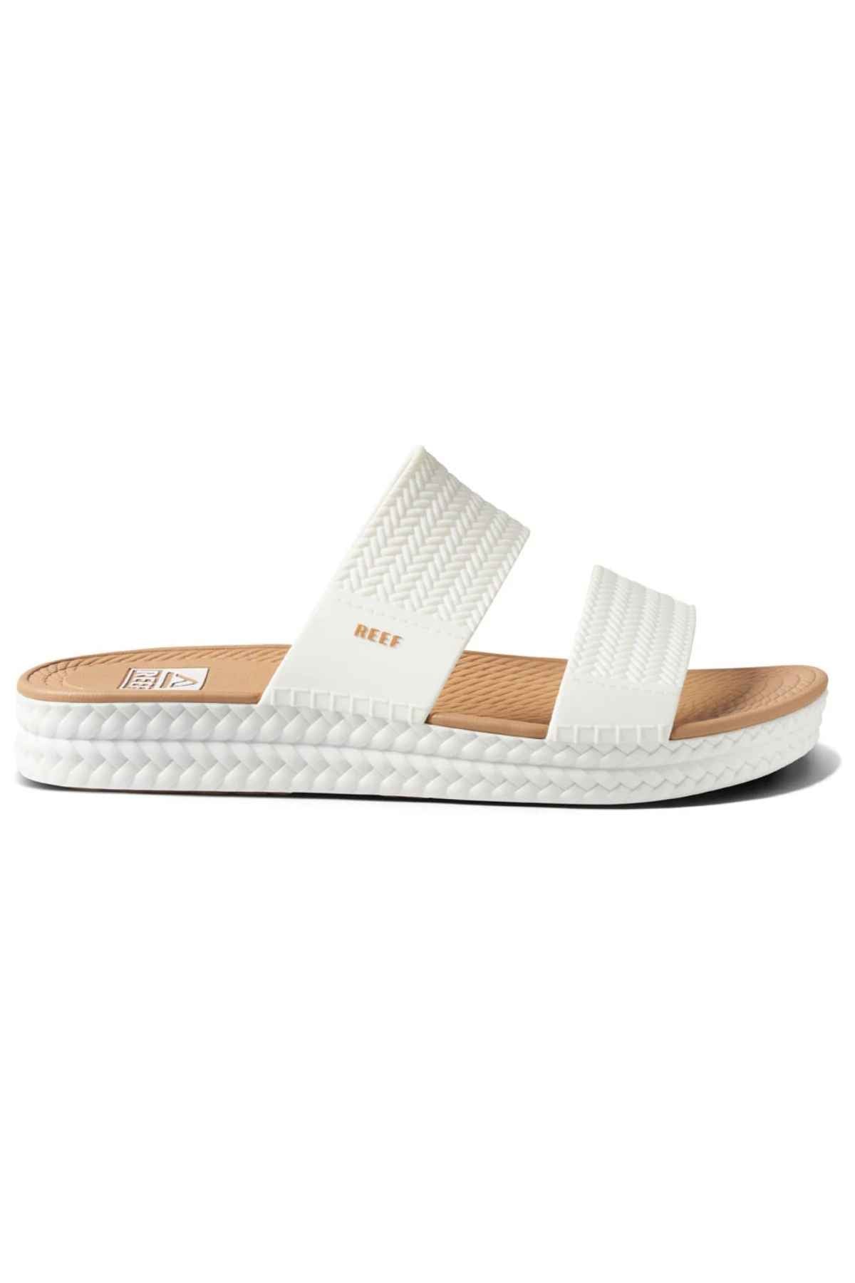 The REEF Water Vista Slide is a white sandal featuring two textured straps, a tan dual density EVA footbed, a white sole with textured edging, and the “REEF” logo on the upper strap.
