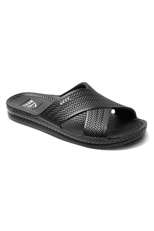 The REEF Water X Slide is a black sandal with a textured woven pattern on the upper strap and footbed, featuring a slightly raised heel and a non-marking sugarcane EVA footbed for comfort. The brand name is elegantly displayed on the strap.