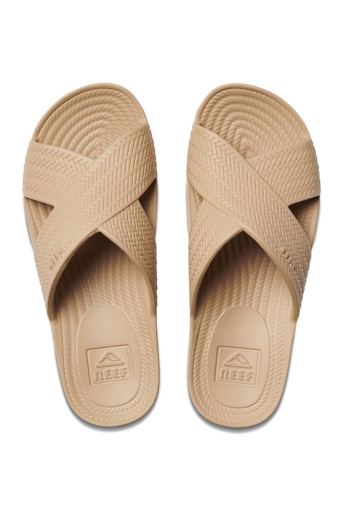 The REEF Water X Slide sandals boast tan waterproof EVA crisscross straps and a patterned sole. Featuring a non-marking sugarcane EVA footbed with the brand logo, they deliver comfort and style for carefree adventures.