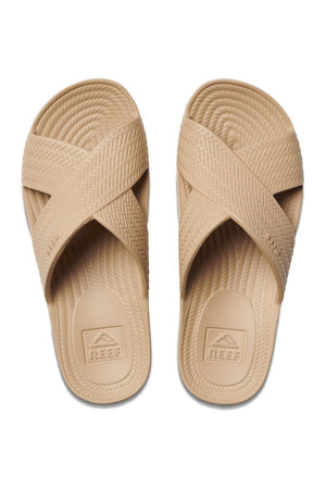 The REEF Water X Slide sandals boast tan waterproof EVA crisscross straps and a patterned sole. Featuring a non-marking sugarcane EVA footbed with the brand logo, they deliver comfort and style for carefree adventures.