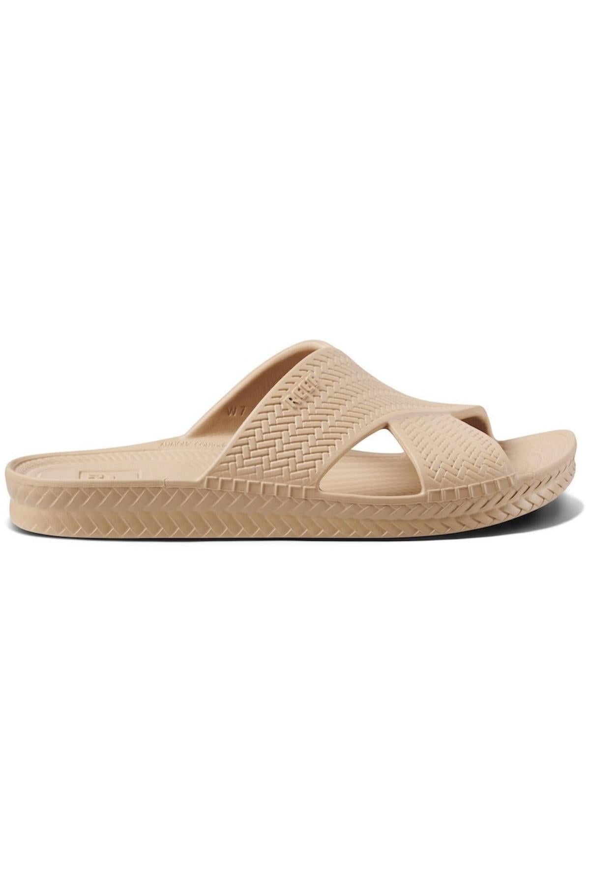 The REEF Water X Slide sandal in beige features a woven texture with a thick cross-foot strap, waterproof EVA straps, and a non-marking sugarcane EVA footbed for comfort and style. A patterned sole border adds elegance.