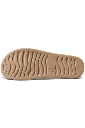 The image displays the REEF Water X Slide's beige shoe sole with a wavy tread for traction, a non-marking sugarcane EVA footbed, and a flat rubber design reflecting its practical style.