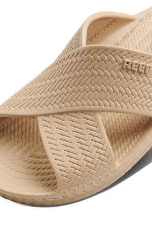 The REEF Water X Slide sandal in beige showcases a woven texture with "REEF" on durable waterproof EVA straps. Its open-toe design includes intersecting straps and a non-marking sugarcane EVA footbed for superior comfort.
