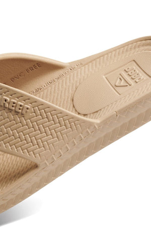 The REEF Water X Slide is a beige sandal with textured, waterproof EVA straps and a woven pattern. It has "Reef" embossed on the side, a non-marking sugarcane EVA footbed, and "PVC Free" marked on the insole.