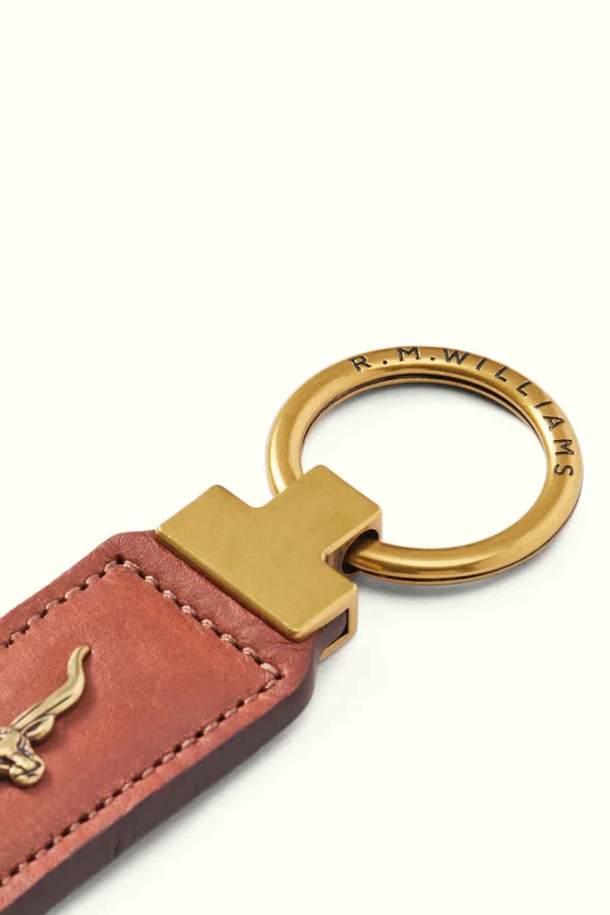 Detailed view of the RM Williams Angaston Key Fob crafted from full-grain leather featuring antique brass hardware. The ring is engraved with "R.M. WILLIAMS," and a small emblem is embossed on the leather section. Made in Australia, it is set against a plain, light-colored background.