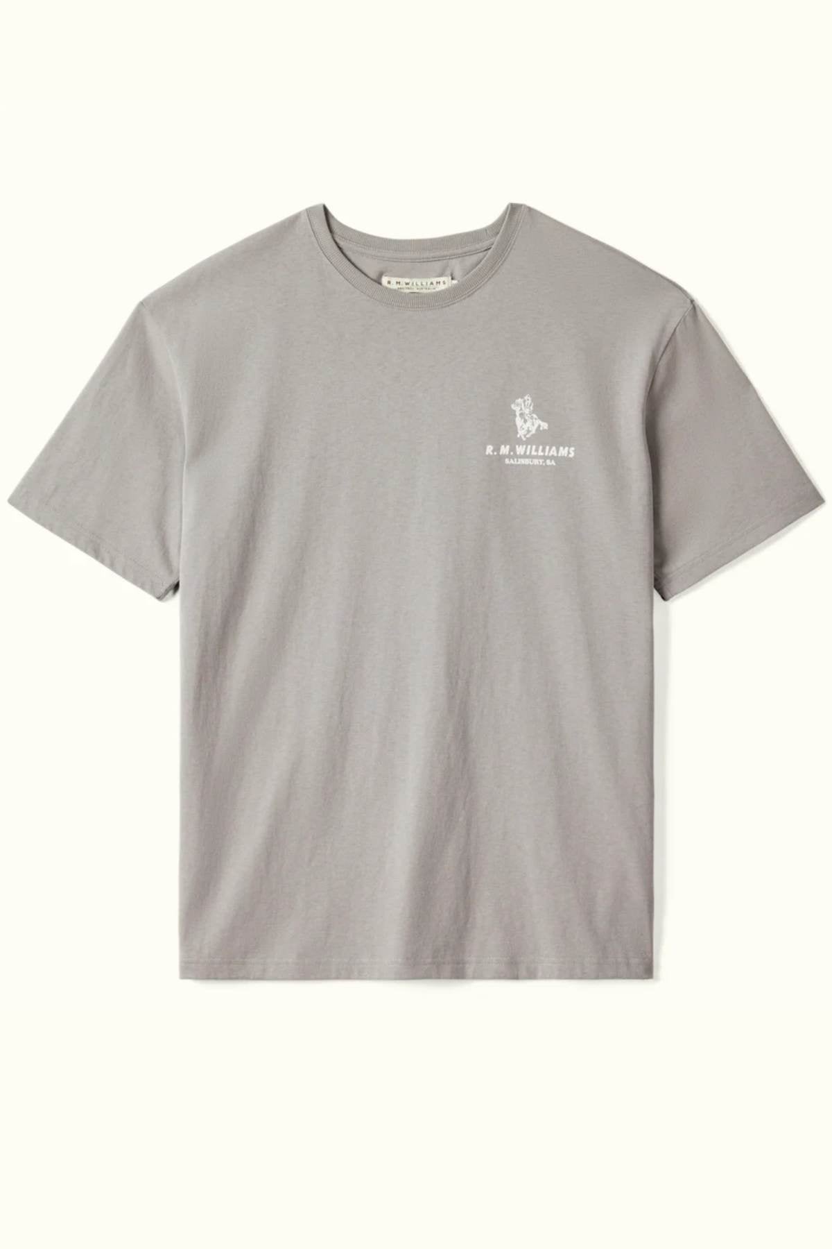 The RM Williams Banner T-Shirt is a gray, short-sleeved garment with a classic round neckline, made from breathable organic cotton for a relaxed fit. It showcases a small white heritage logo on the upper left side, featuring "R.M. WILLIAMS" accompanied by a graphic above the text, all set against a plain light background.