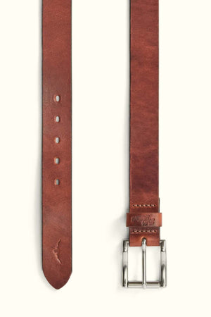 The RM Williams Berwick Belt is shown laid flat, featuring brown leather, a silver roller buckle, punched holes and pointed tip on one end, with embossed branding near the leather keeper on the other.