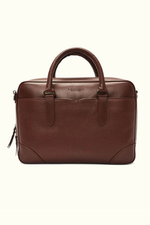 The RM Williams Briefcase is a refined accessory in brown full grain leather, featuring a textured finish, two sturdy handles, a discreet logo near the top, dark edge accents, and a zipper closure with dual pull tabs.