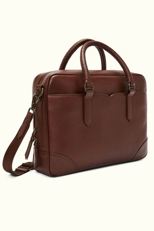 The RM Williams Briefcase is a men's accessory crafted from full-grain leather with a sleek, smooth texture. It includes a shoulder strap, two top handles, and a front pocket. Metallic zippers and hardware add to its classic and professional appeal.