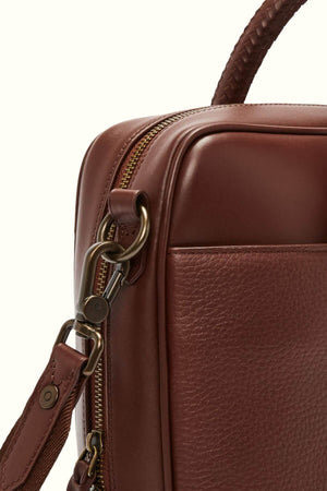 Close-up of a stylish men's RM Williams Briefcase crafted from full grain brown leather with a textured design. The image highlights a metal zipper, detachable strap with clasp, and clearly visible stitching and texture.