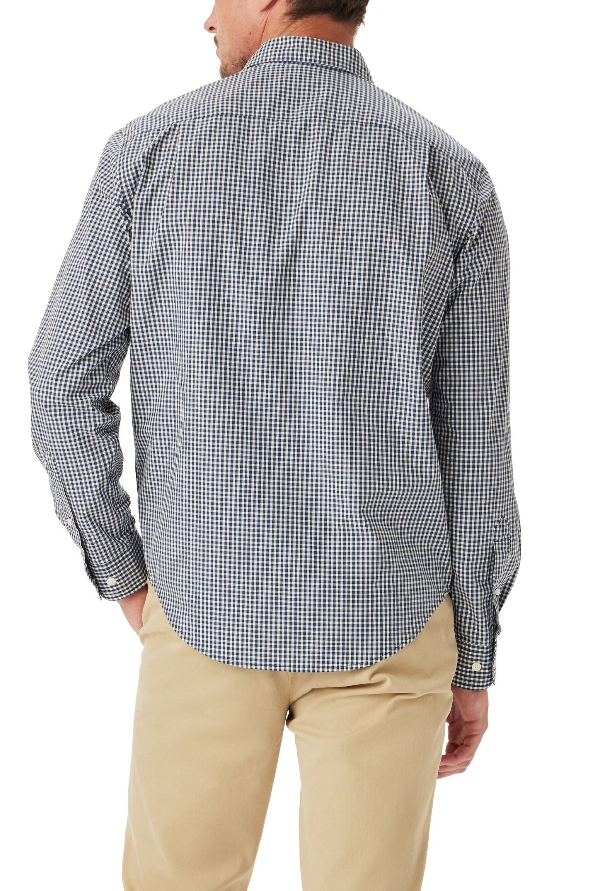 A man stands facing away in the RM Williams Classic Poplin Check Shirt, a black and white organic cotton, yarn-dyed check shirt with long sleeves, paired with beige pants. His left hand is in his pocket and only part of his face is visible.