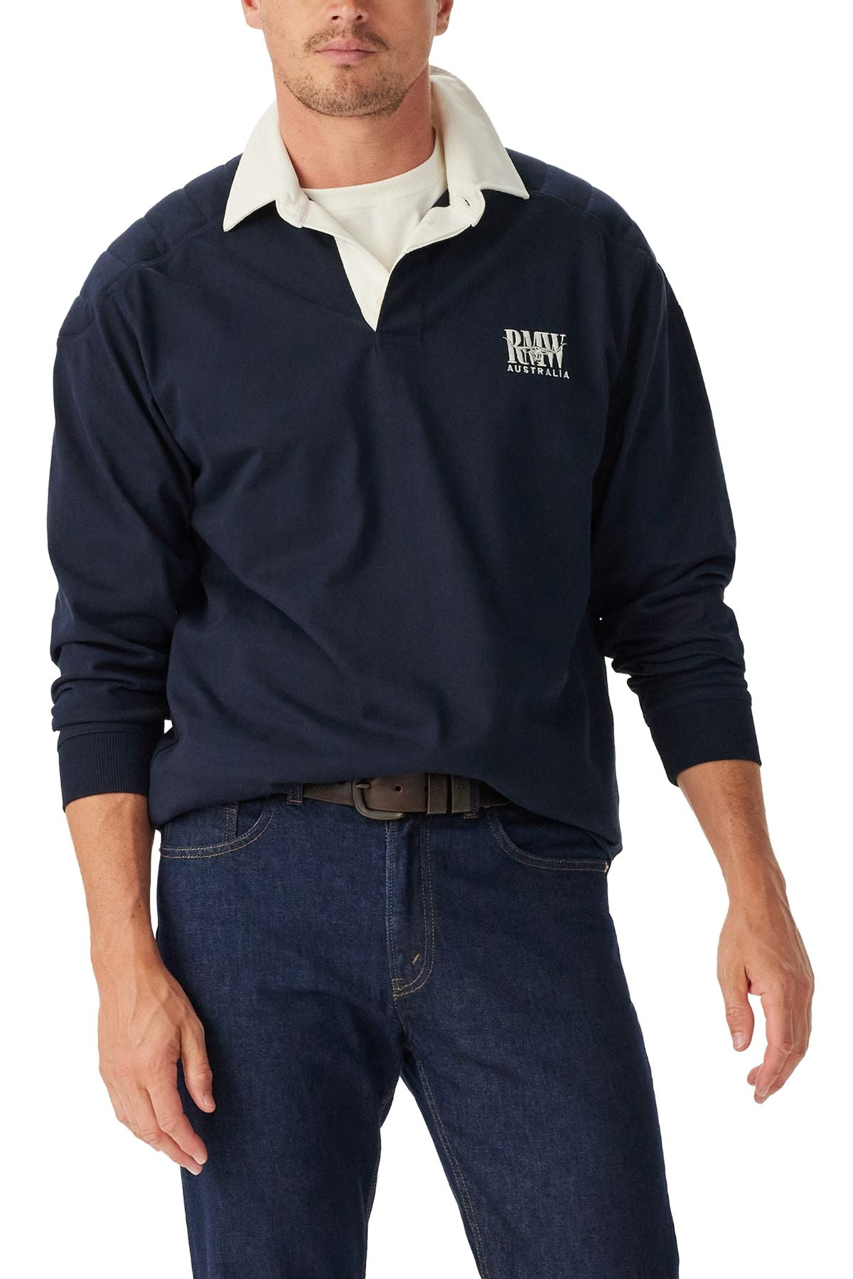 A man wears a navy RM Williams Classic R.M.W Rugby shirt with a white collar and "RAW AUSTRALIA" on the left chest, paired with dark blue jeans and a brown belt. His face is partially out of frame.