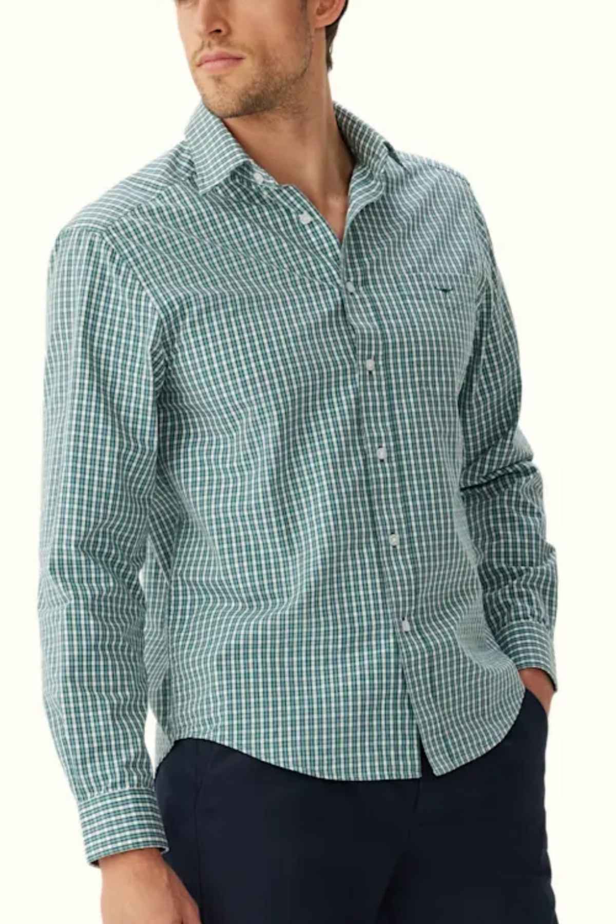 A man is wearing a RM Williams Classic Shirt in green and white gingham check, paired with dark blue pants. His hand is in his pocket as he looks to the side.