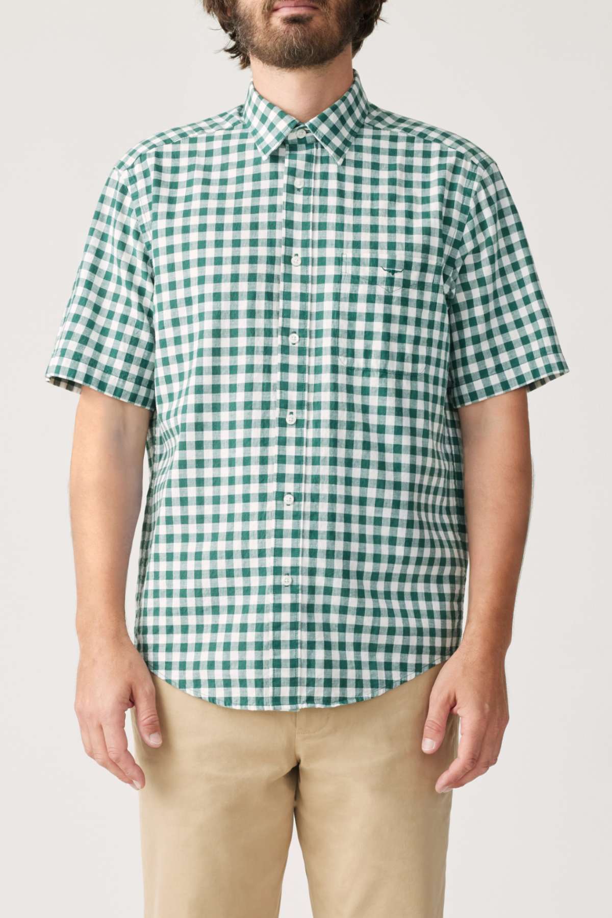 A person wearing the Classic Short Sleeve Shirt from RM Williams, featuring a green and white gingham pattern, with beige pants stands against a plain background. Their face is not visible.