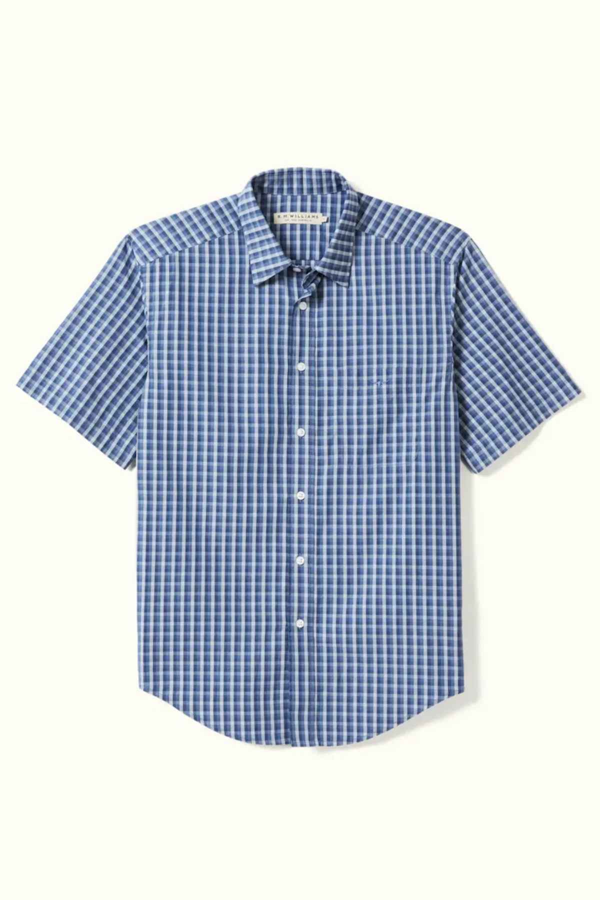 The RM Williams Classic Short Sleeve Shirt, displayed against a light background, features a blue and white checkered pattern. Made from soft cotton poplin, it boasts a standard collar, a chest pocket on the left side, and offers a comfortable regular fit.