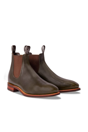 The RM Williams Comfort Craftsman Boot in olive green pull-up leather features brown elastic side panels, brown soles, and back pull tabs—crafted in Australia and shown against a white background.