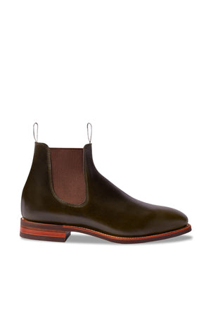 The RM Williams Comfort Craftsman Boot, in dark green pull-up leather with brown elastic side panels, pull tabs, and a brown stacked heel, is shown on a white background.