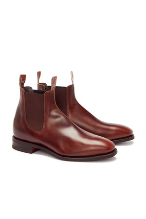 The RM Williams Comfort Craftsman Boot is a brown yearling leather Chelsea boot with elastic side panels, pull tabs, low stacked heels, and a durable rubber welt sole, shown on a white background.