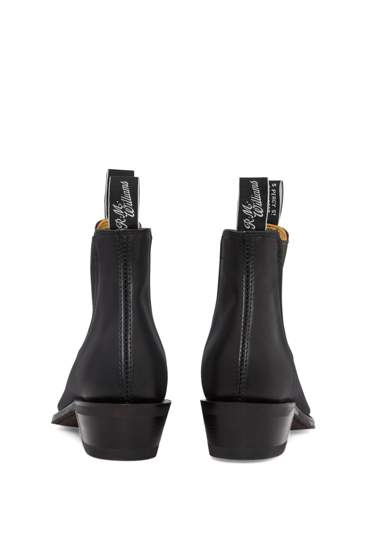 Back view of the RM Williams Comfort Lady Yearling Rubber Sole Boot in black leather, displaying text on the pull tabs. These elegant Chelsea boots are made from Yearling leather, featuring elastic sides, a small block heel, and visible stitching.