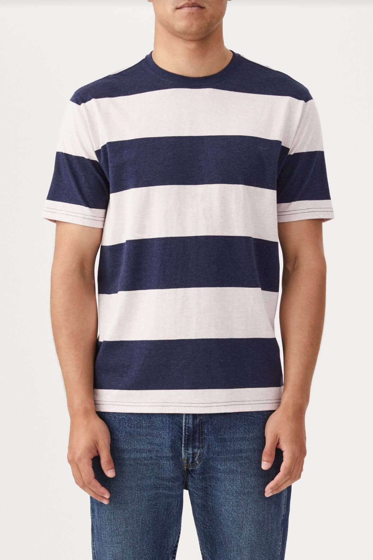 A person wears the RM Williams Copley short-sleeved, navy and white striped cotton T-shirt, paired with blue jeans against a plain background. Their hands rest by their sides, and the head is not visible in the image.