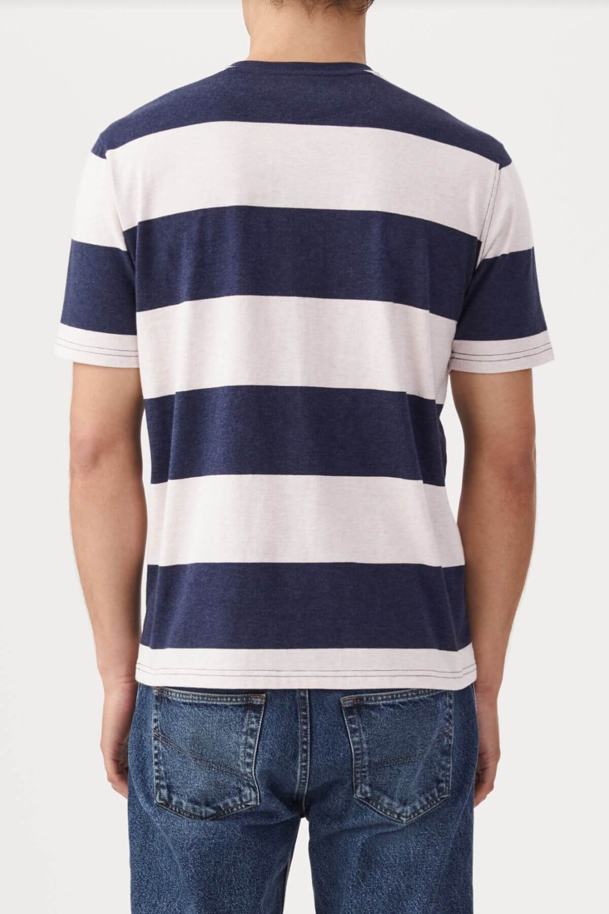 Rear view of a person in a RM Williams Copley T-Shirt, featuring navy and white broad horizontal stripes, short sleeves, and classic striped style. They are wearing blue jeans against a plain white background.