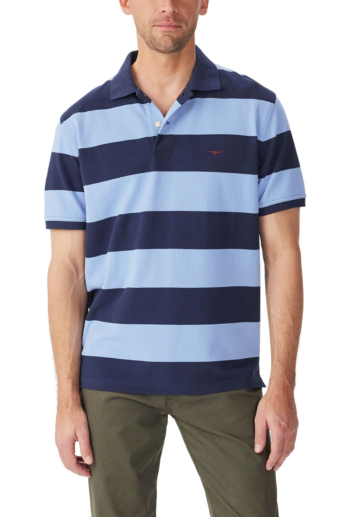 A man wears the RM Williams Craddle Polo, crafted from organic cotton with wide navy and light blue stripes, a small red chest logo, paired with olive green pants.