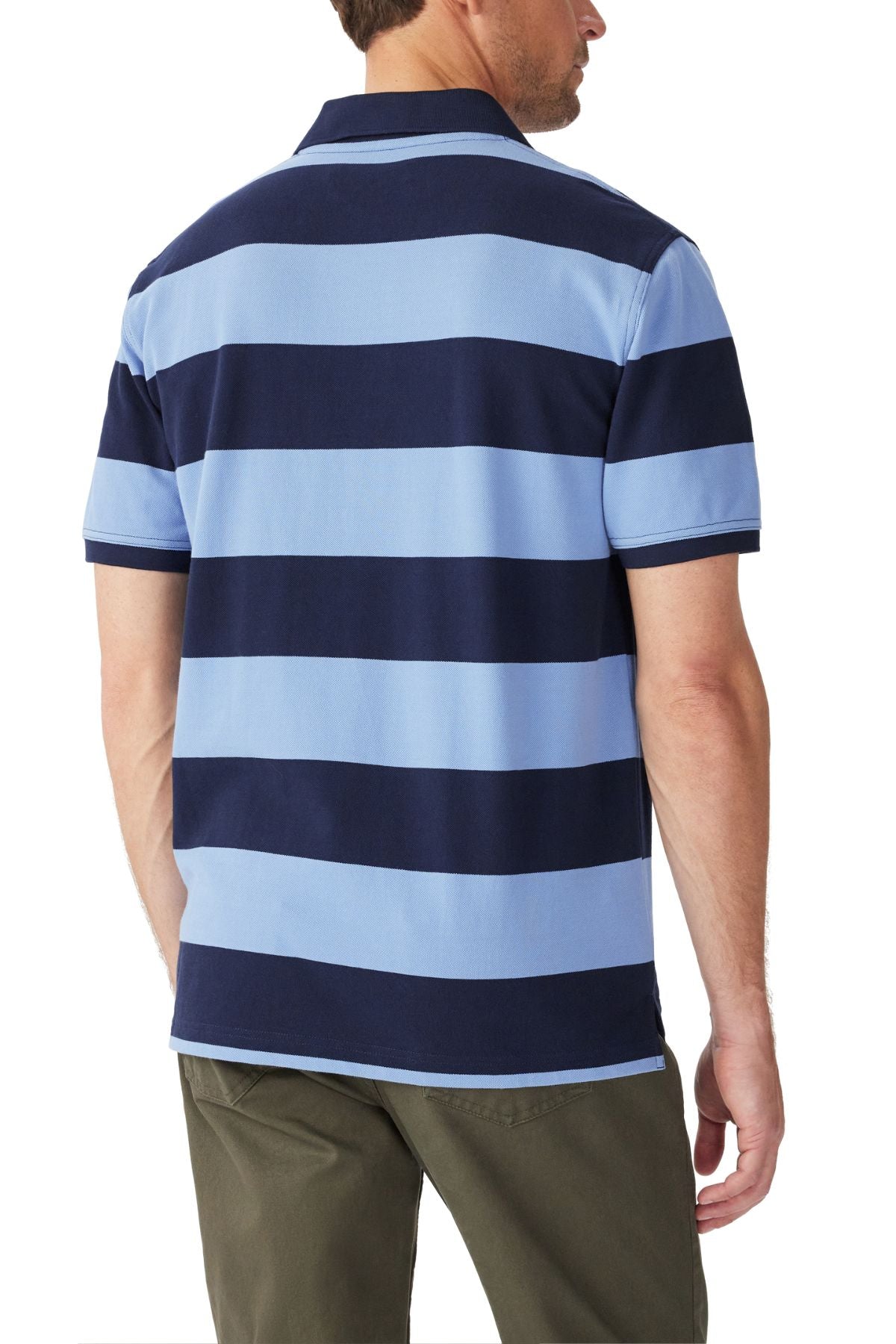 A man is shown from the back wearing the RM Williams Craddle Polo, a short-sleeve collared rugby shirt with wide navy and light blue stripes in organic cotton, paired with olive green pants.