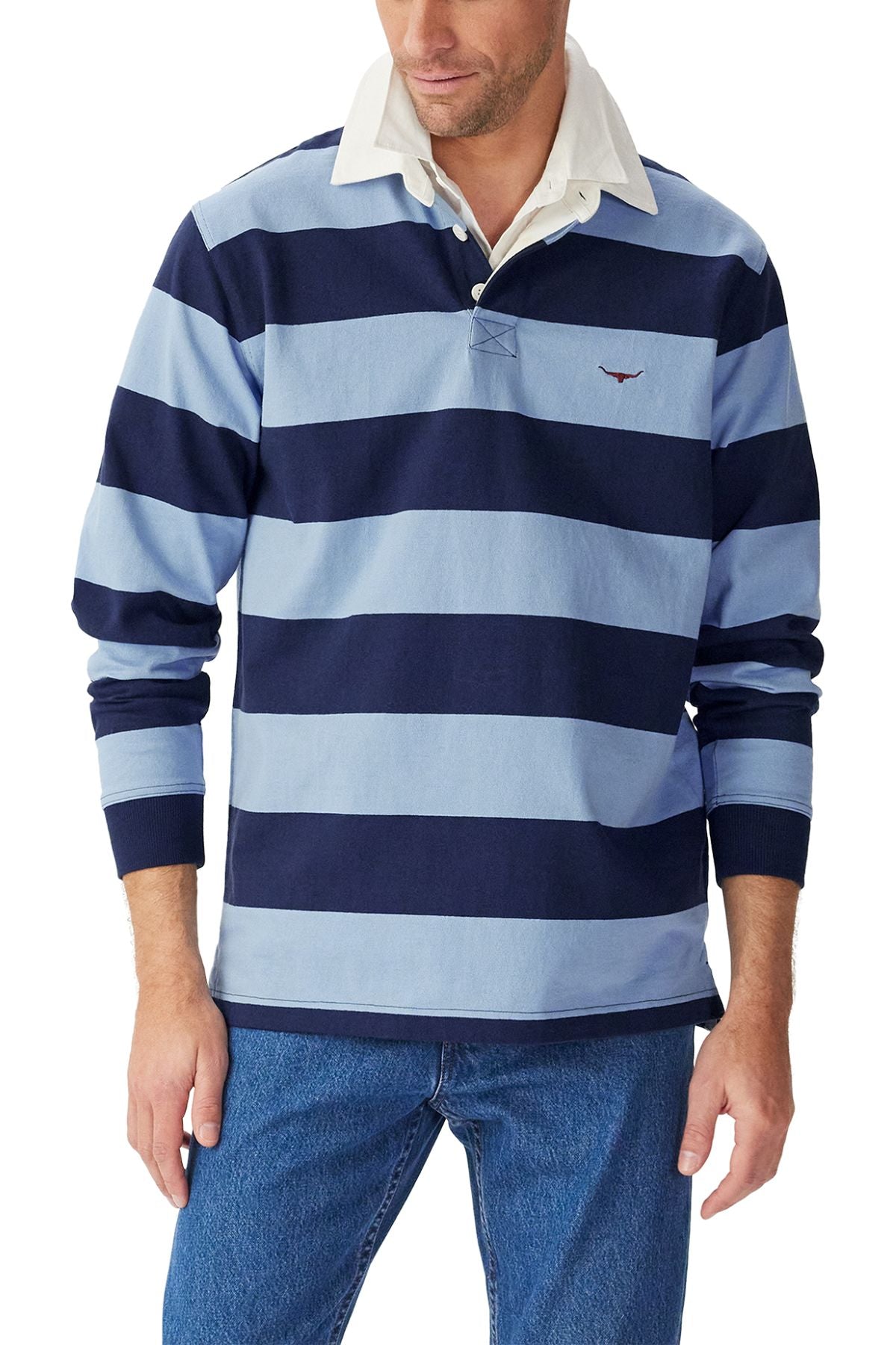 A man wears the RM Williams Cradle Rugby, an organic heavyweight striped rugby shirt with a white collar, paired with blue jeans. He stands with his hands at his sides and his face partially visible.