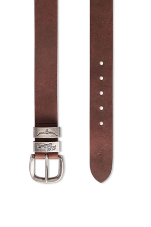 The RM Williams Drover Belt, a brown Crazy Horse Leather accessory featuring a silver buckle, is displayed against a white background. The belt, handmade in Australia, includes five adjustment holes. One end sports the buckle and a loop with text, while the other end tapers to a point and has a small mark near the bottom hole.