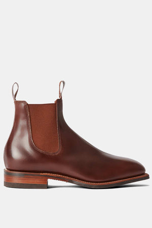 The RM Williams Dynamic Flex Craftsman Boot is a brown handcrafted leather Chelsea boot with a sleek design, elastic side panels, pull tabs, rounded toe, and stacked heel. It features a durable leather and rubber sole on a plain grey background.