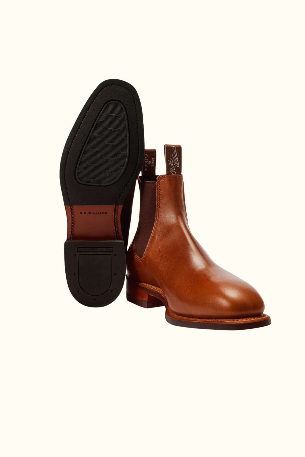 The RM Williams Dynamic Flex Craftsman Boot, made from yearling leather, is displayed on a light background with one boot upright and the other sole-up to reveal its black sole and branded pull tabs.