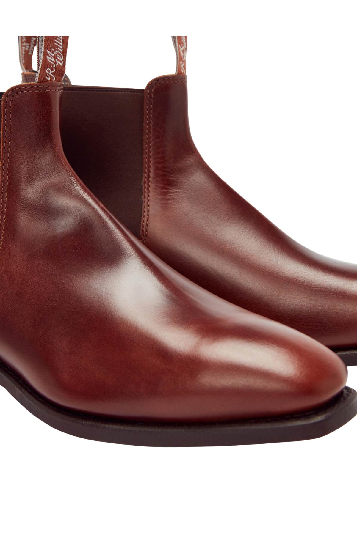 Close-up of a pair of RM Williams Dynamic Flex Craftsman Boots made from polished brown yearling leather, showcasing their elastic side panels and sleek design. These boots have a smooth finish and are elegantly displayed on a white background.