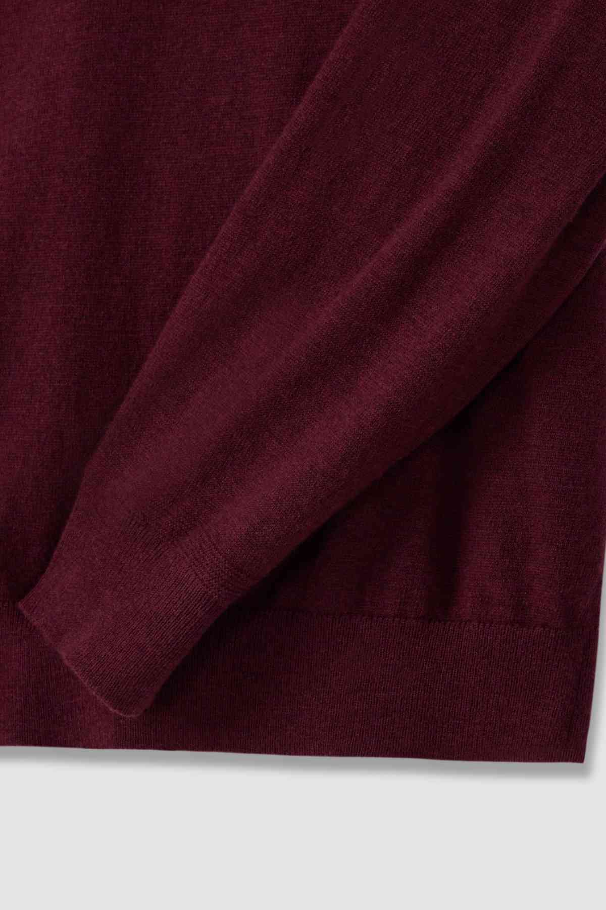 Close-up of an RM Williams Ernest Sweater in burgundy merino wool. The fine gauge fabric is soft and cozy with ribbed wrist cuffs. Its rich color implies warmth and comfort, perfect for a quarter zip sweater.