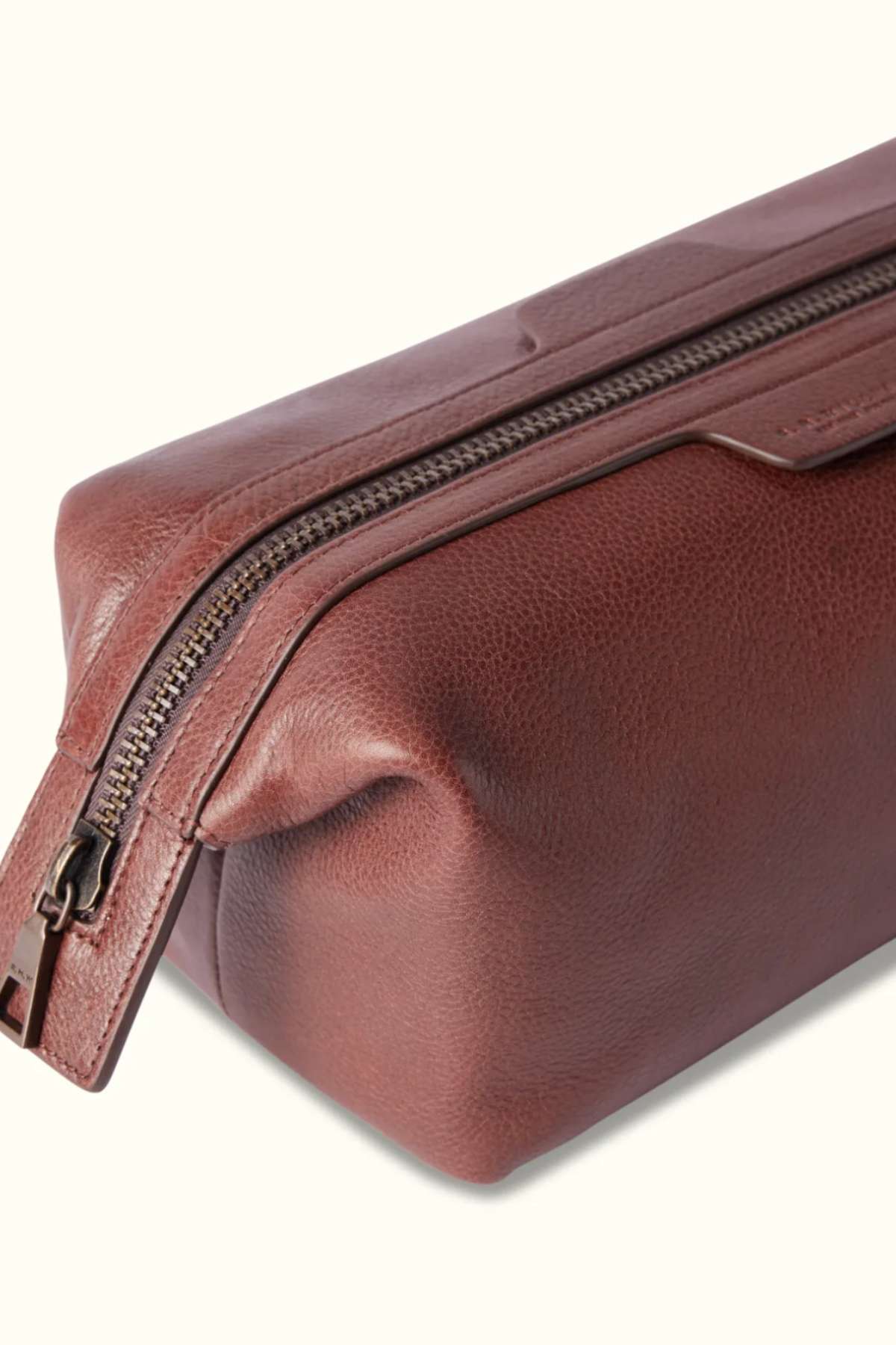 The RM Williams Farrier Washbag, a brown tumbled grain leather washbag with a smooth finish and partially open visible top zipper, is showcased against a light background in a rectangular shape.