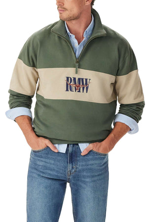 A man wearing a green and beige RM Williams Heritage 1/4 Zip Sweatshirt with "PMV RW" on the front, a light blue collared shirt underneath, and blue jeans has his hands in his pockets.
