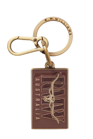 The RM Williams Heritage Logo Enamel Key Ring features a rectangular brown tag with "R.M.W. AUSTRALIA" and a longhorn outline, plus round brass hardware engraved with "R.M.WILLIAMS.