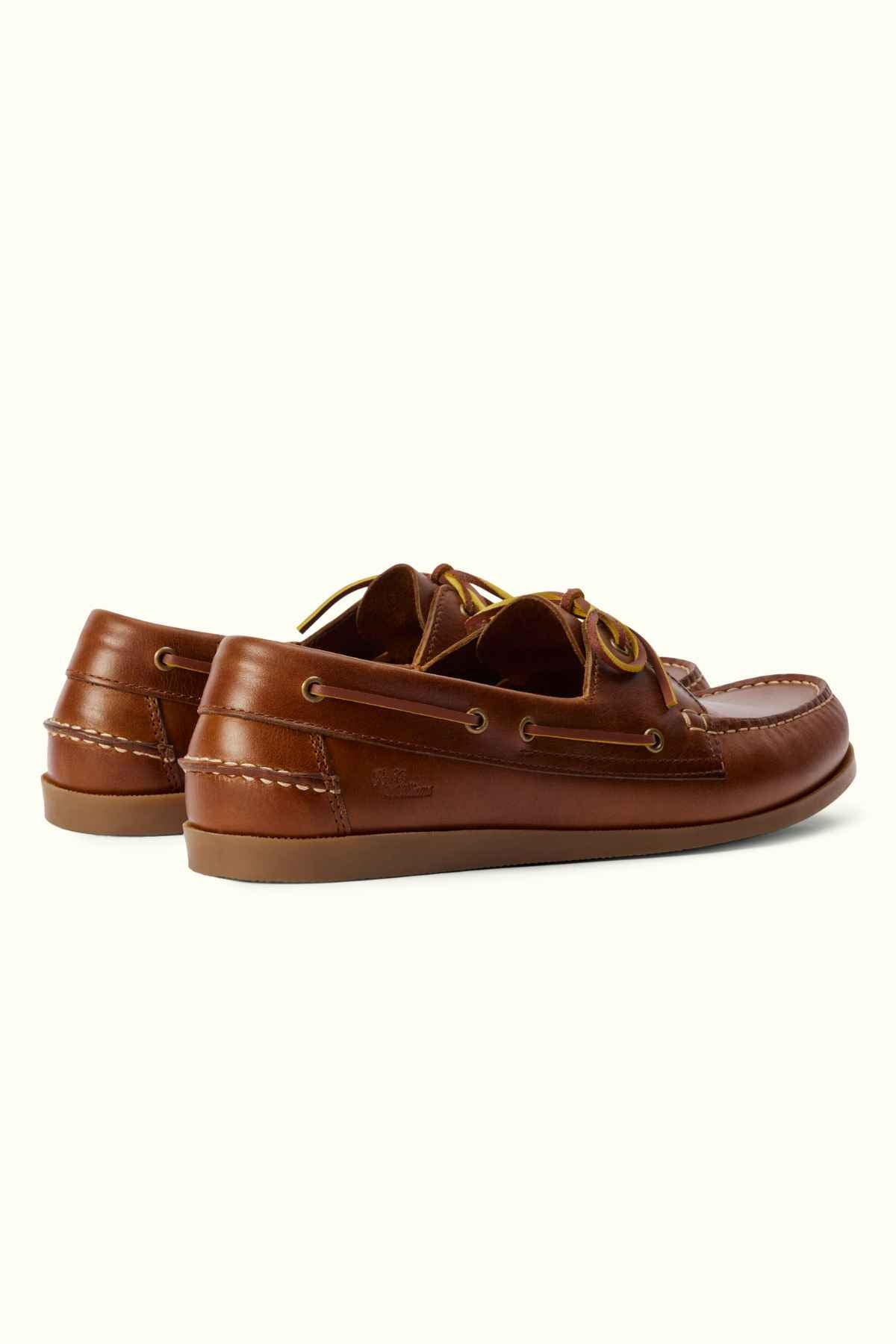 A pair of RM Williams Islet Moccasin in brown leather, featuring laces and detailed stitching. These moccasins boast a classic design with eyelets and a moc-toe front. The flat soles and small decorative laces threaded through metal eyelets on the sides complete their timeless look.