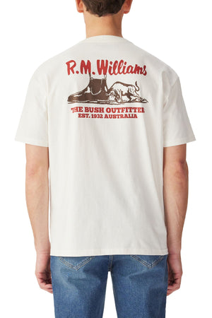 Man wearing the RM Williams Last T-Shirt in white, featuring red text and brown boot and dog graphics on the back: "R.M. Williams, The Bush Outfitter, Est. 1932 Australia." Check our size guide for accurate chest measurements.