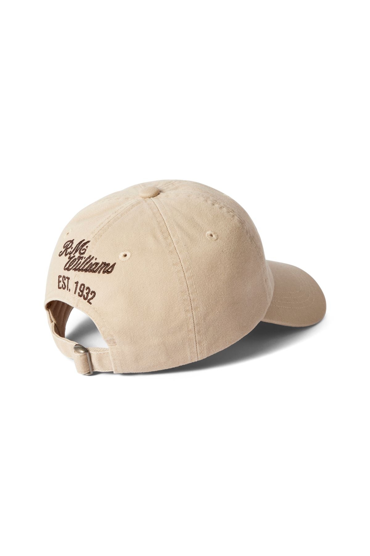 The RM Williams Longhorn Twill Cap is a beige baseball cap made from organic cotton twill, shown from the back with "Billionaire" and "EST. 1932" embroidered in brown above the adjustable strap.