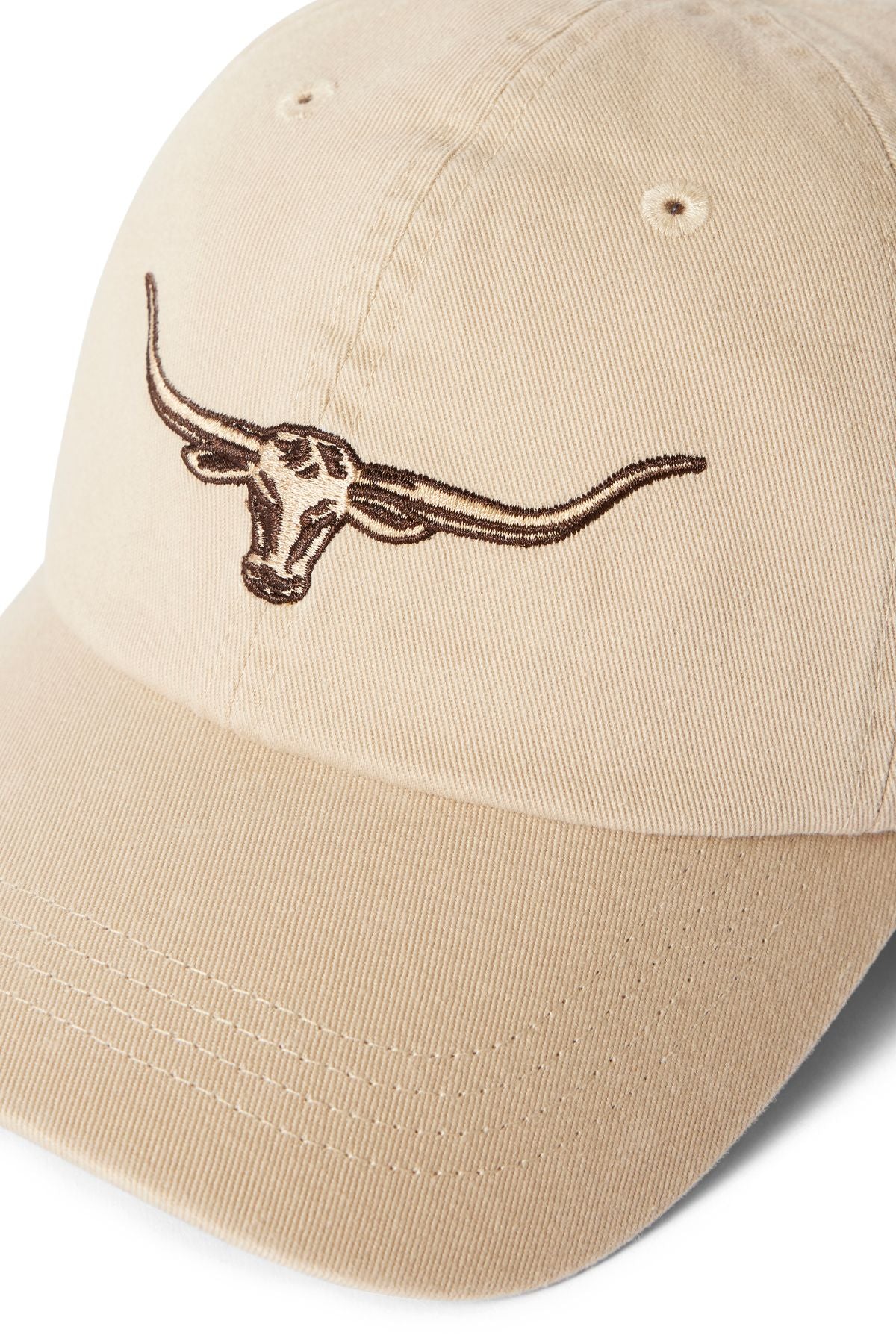 The RM Williams Longhorn Twill Cap is made from organic cotton twill in beige, featuring a brown embroidered steer head on the front. It includes an adjustable strap and ventilation eyelets for comfort and a secure fit.