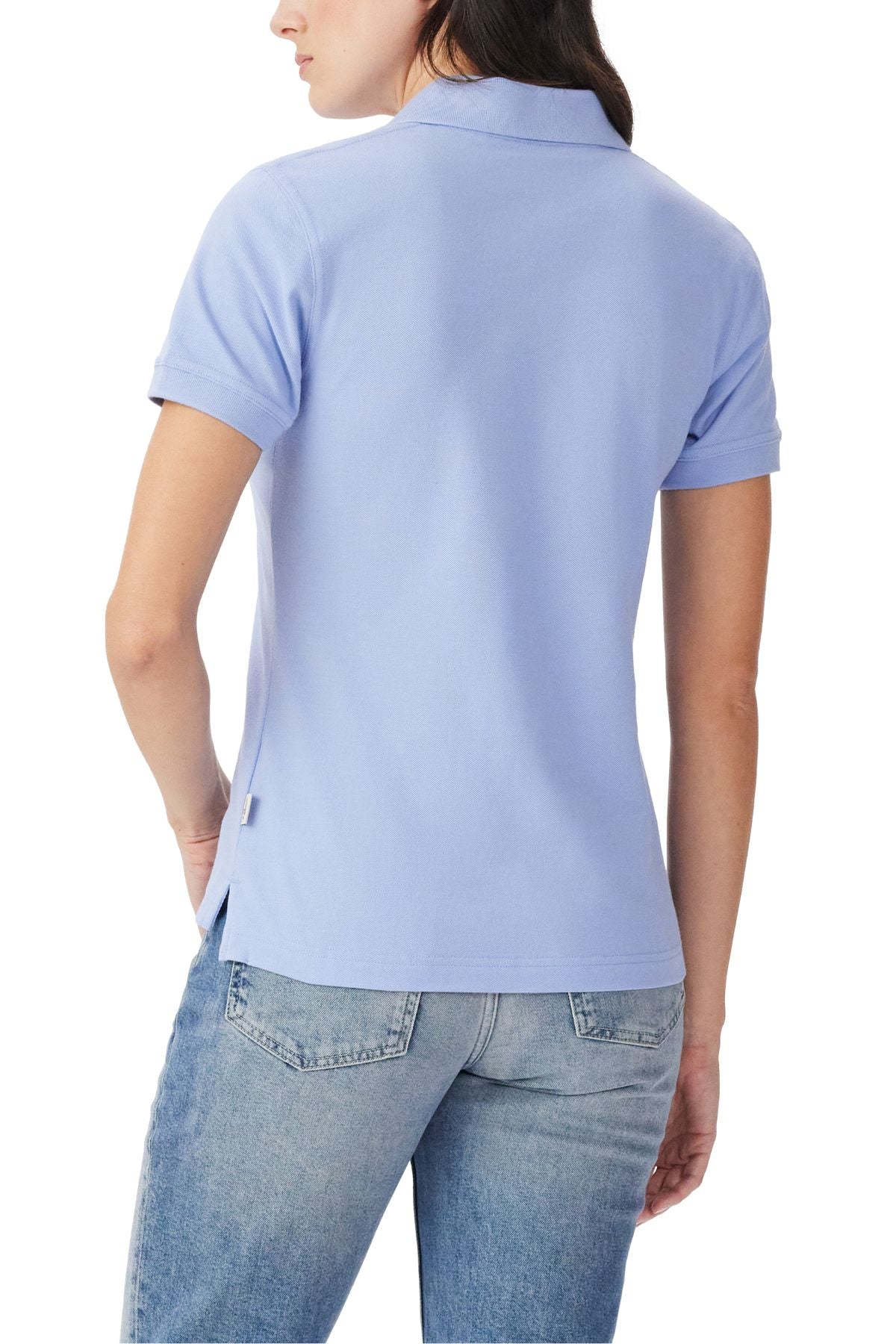 A woman is shown from the back wearing the RM Williams Margaret Polo in light blue, with short sleeves and Longhorn embroidery, paired with light-wash jeans and her left hand in her pocket.