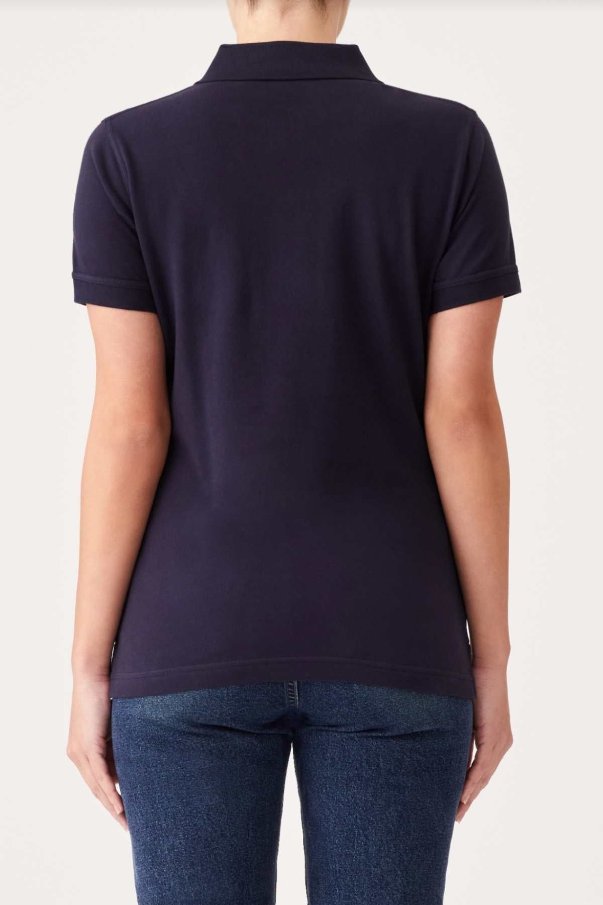 A person wearing a plain black RM Williams Margaret Polo with short sleeves and blue jeans stands facing away, showcasing the back of the outfit. The image highlights their upper and lower back against a simple off-white background.