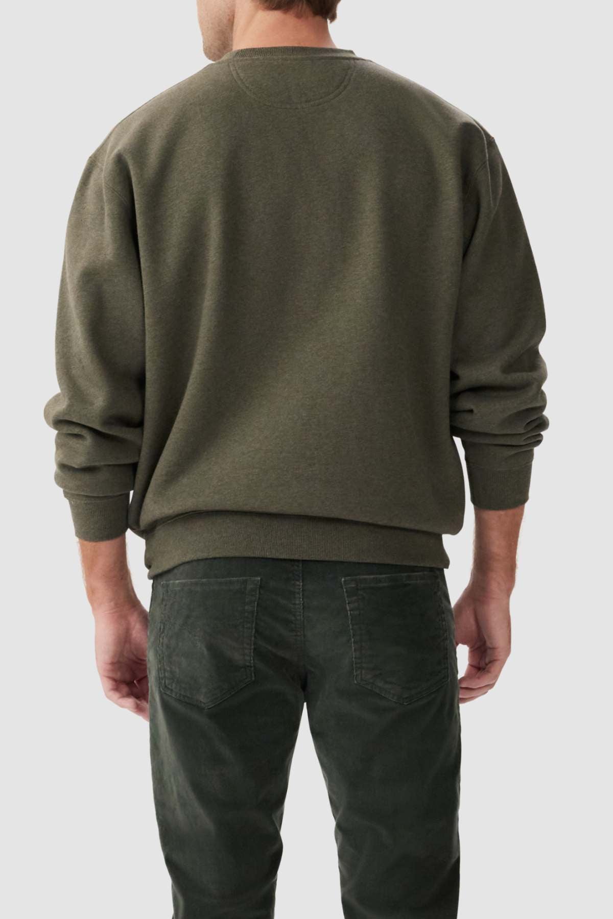 A person wearing a green RM Williams Mini Longhorn Sweatshirt and matching green pants is standing with their back to the camera against a plain gray background. The sleeves of their crew neck fleece sweatshirt are slightly pushed up.
