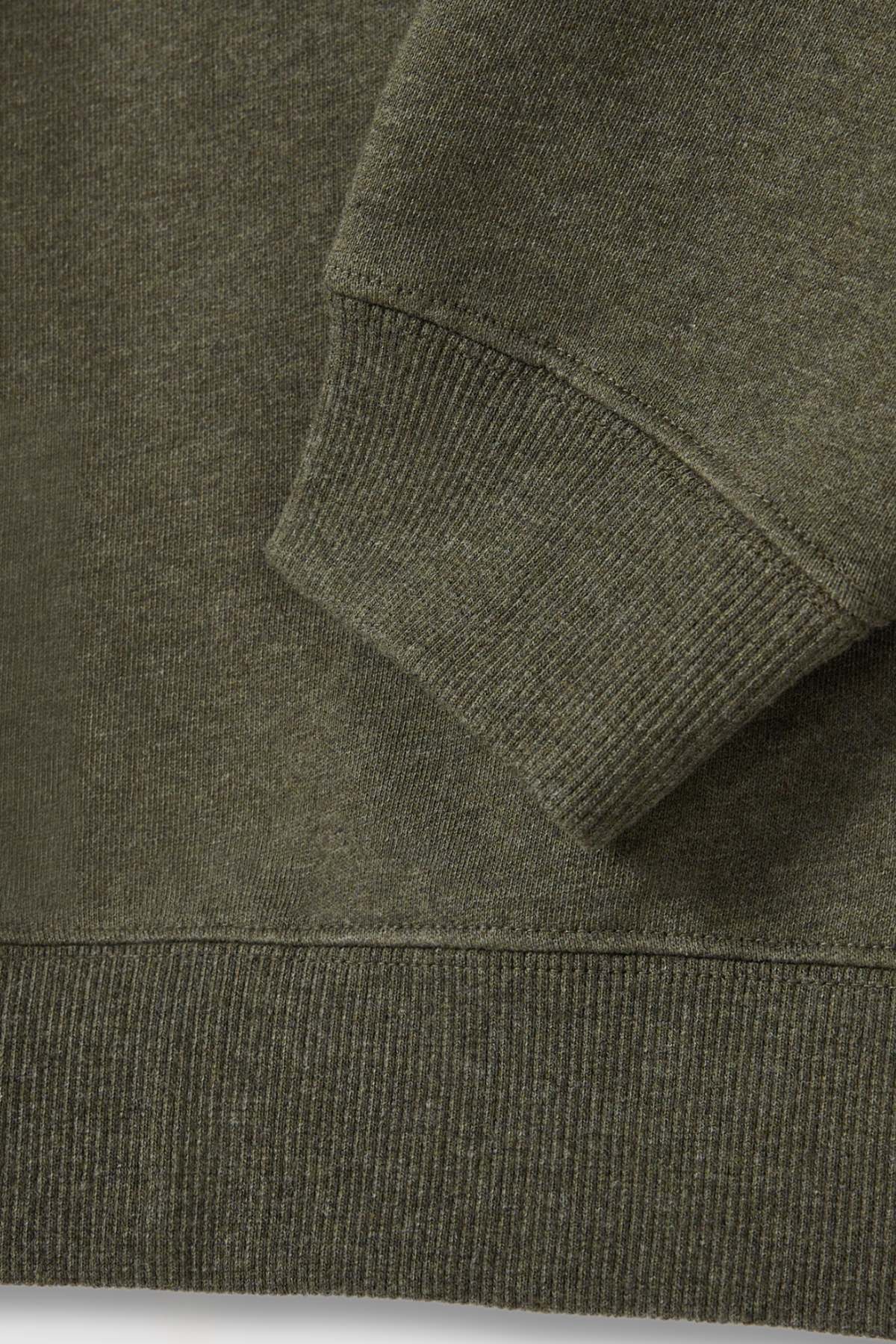 Close-up of the RM Williams Mini Longhorn Sweatshirt's sleeve and bottom hem. The fabric appears to be knitted, with ribbed cuff and hem providing a textured look. Made from recycled cotton poly fleece, its earthy olive green hue gives it an eco-friendly charm.