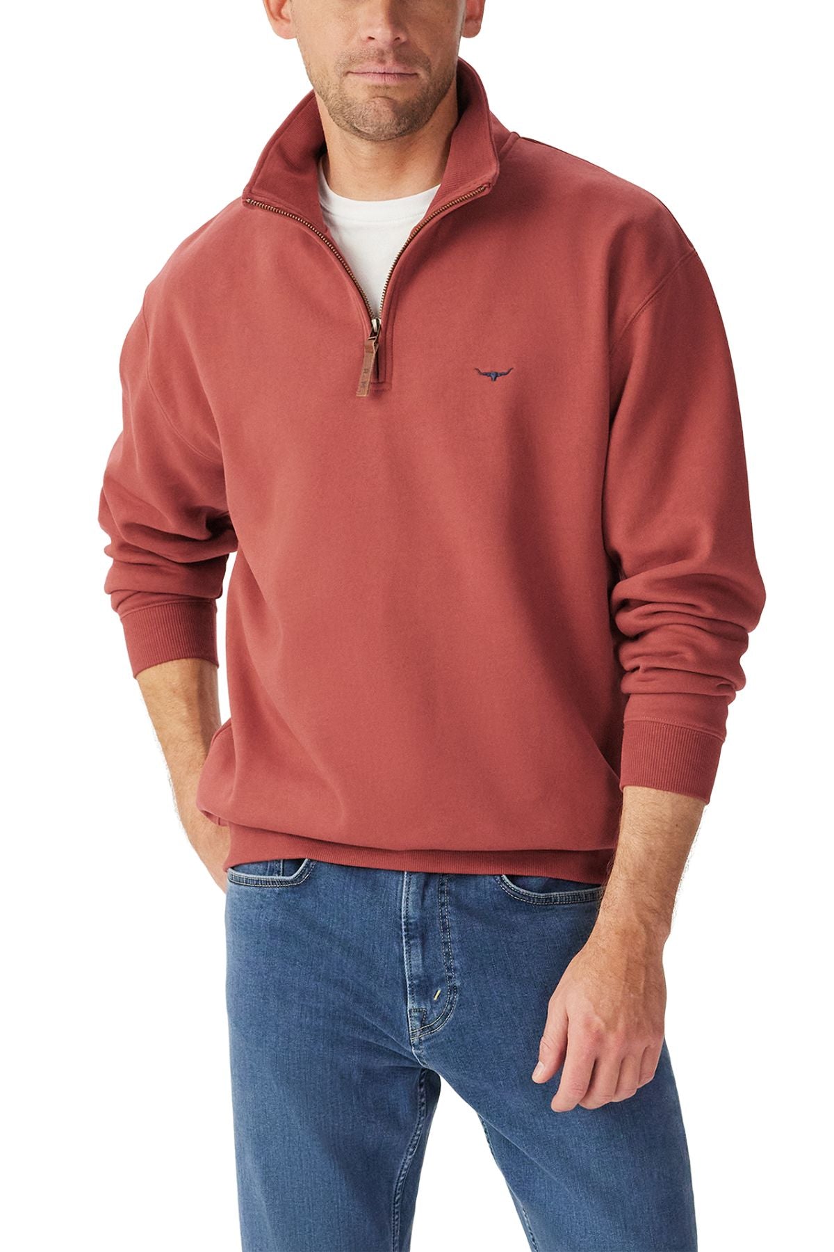 A man wears the rust RM Williams Mulyungarie Fleece quarter zip over a white T-shirt and blue jeans, standing with one hand in his pocket against a plain white background.