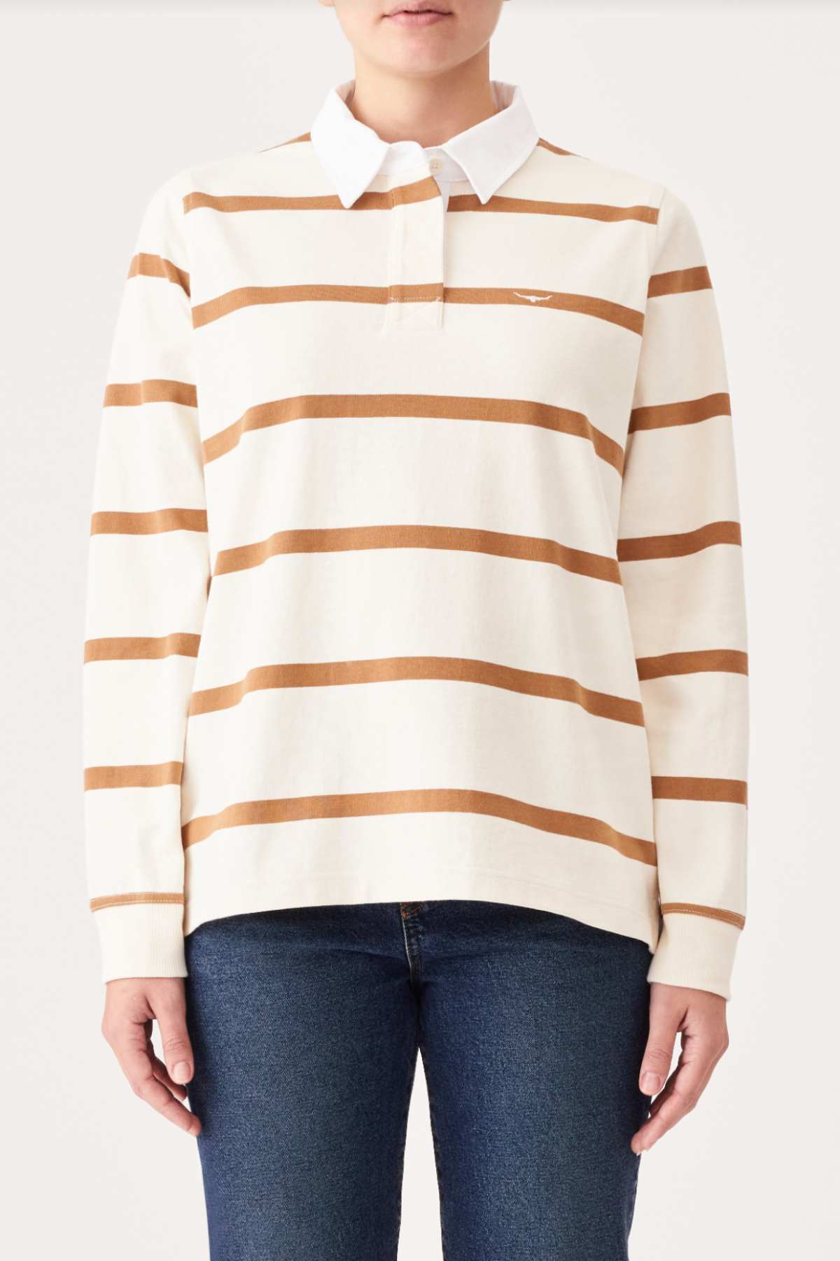 A person wearing an RM Williams Nundle Rugby shirt, featuring long sleeves with white and beige stripes and a white collar, paired with blue jeans. The photo is taken from the front, showing the upper body and partially the legs against a plain background.