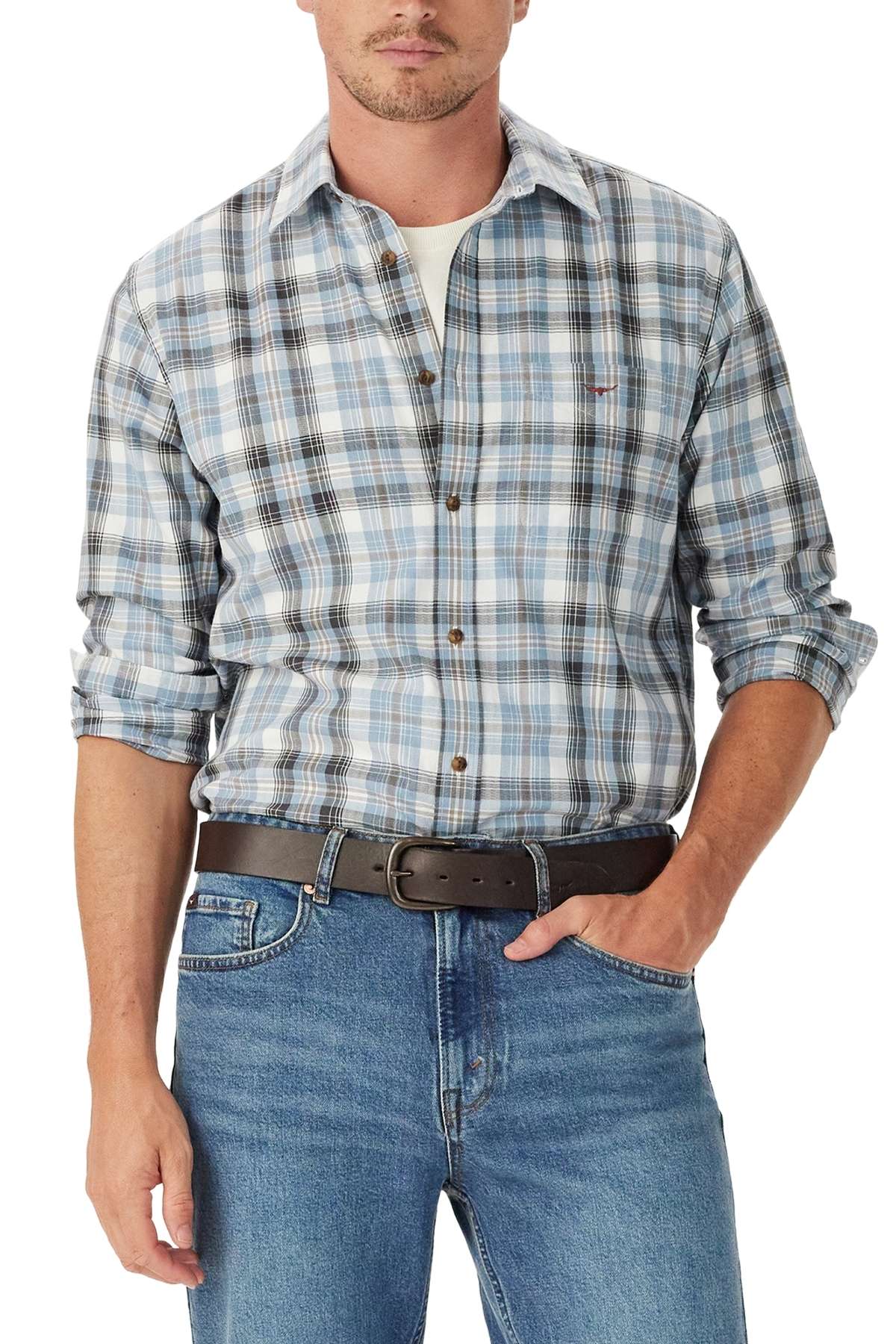 A man wears the RM Williams O'Connell Check Shirt in blue and gray plaid over a white T-shirt, paired with blue jeans and a black belt. His sleeves are rolled up, left hand in his pocket, with his face partially visible.
