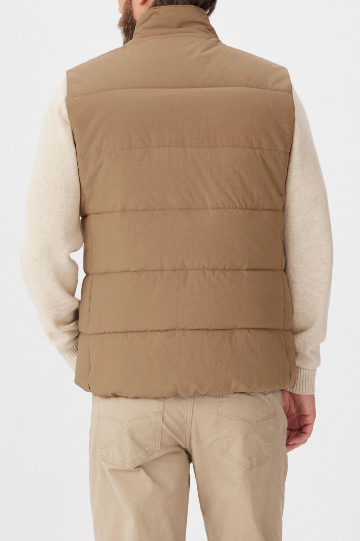 A person is shown from behind wearing the RM Williams Padstow Vest in tan, made from recycled nylon, over a light beige long-sleeve shirt and beige pants against a plain white background.