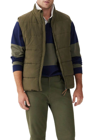 A person wearing an RM Williams Padstow Vest in green with PrimaLoft filling over a green and navy striped long-sleeve shirt. They are also dressed in green pants and posed against a plain white background.